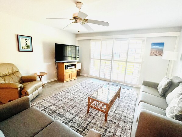 A living room with a sofa, armchair, coffee table, TV stand, and a ceiling fan.
