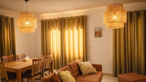 A living room with a brown sofa, wooden dining table, chairs, and two hanging wicker lamps.