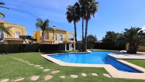 A swimming pool surrounded by well-maintained grass and palm trees, with a yellow building in the background.