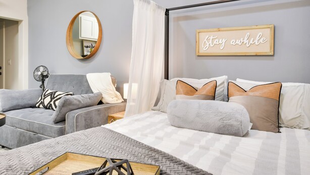 A modern bedroom with a bed, a grey sofa, a small table, and a mirror. - Relaxing Lubbock Studio ~ 6 Mi to Texas Tech (Lubbock)