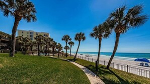 Un sendero bordeado de palmeras que conduce a una playa, con un edificio al fondo.