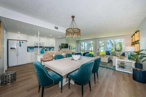 Una cucina moderna con mobili bianchi, un'area pranzo con sedie color petrolio e un'ampia finestra che offre luce naturale.