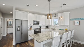 A modern kitchen with white cabinets, granite countertops, stainless steel appliances, and a central island with bar stools. - Fond Horizons: Beach View, Private Pool, Pet Friendly! (Cape San Blas)