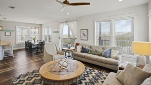 A spacious living room with a dining area, large windows, and a ceiling fan. - Fond Horizons: Beach View, Private Pool, Pet Friendly! (Cape San Blas)