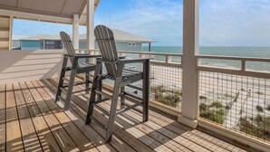 Una terraza de madera con sillas Adirondack que da a una playa con cielo despejado.