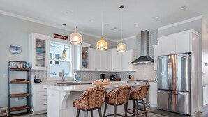 Una cocina moderna con armarios blancos, un refrigerador de acero inoxidable y tres taburetes de mimbre.