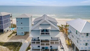 Una propiedad frente a la playa con varias construcciones, entre ellas una casa blanca destacada con techo a dos aguas y una casa azul más pequeña.