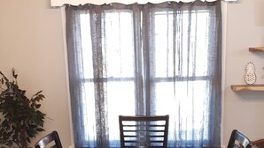 A dining room with a rectangular table, four chairs, a chandelier, a potted plant, and a window with curtains. - The Cam Grady, Restored, roomy, eclectic cottage in heart of Downtown Morganton (Morganton)