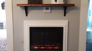 A fireplace with a mantel shelf displaying a framed picture and a small model tower. - The Cam Grady, Restored, roomy, eclectic cottage in heart of Downtown Morganton (Morganton)