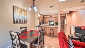 Un coin repas avec une table et des chaises en bois, un tapis rouge et un tableau représentant des arbres.