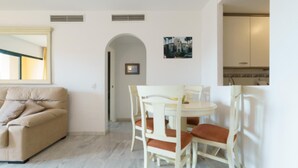 Un salon avec un canapé beige et un coin repas comprenant une table et des chaises blanches.