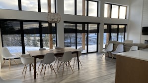A spacious modern kitchen with large windows, a dining area with a wooden table and chairs, and a cozy seating area with a sofa and chairs. - Modern three bedroom with Panoramic Oceanview  (Hubbards)