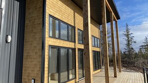A modern two-story building with large windows and a wooden deck. - Modern three bedroom with Panoramic Oceanview  (Hubbards)