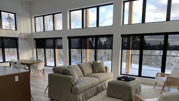 A spacious living room with a large window overlooking a snowy landscape, a wooden dining table, and a modern sofa. - Modern three bedroom with Panoramic Oceanview  (Hubbards)