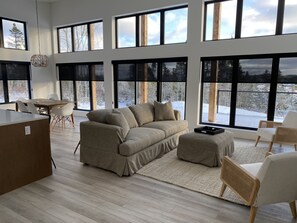 Un salón espacioso con un gran ventanal con vistas a un paisaje nevado, una mesa de comedor de madera y un sofá moderno.