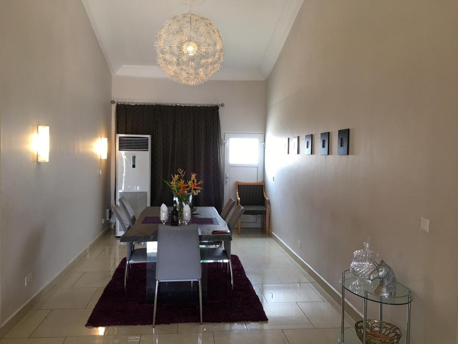 A dining area with a table set for four, a chandelier, and a window with curtains.