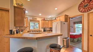 Una cocina con armarios de madera, una isla grande con taburetes, un refrigerador y un reloj en la pared.