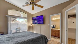 Une chambre avec un lit, un ventilateur de plafond, une télévision et une vue sur un barbecue situé à l’extérieur.