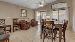 Un vaste espace de vie comprenant une table à manger, des chaises, un ventilateur de plafond et une grande fenêtre.