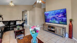 Un salon avec un canapé, un téléviseur, un ventilateur de plafond et un vase de fleurs.