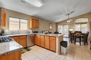A kitchen with wooden cabinets, a granite countertop, a gas stove, and a dining area with a table and chairs.