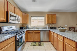 A kitchen with wooden cabinets, a microwave, stove, dishwasher, and a window with blinds.