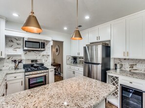 A modern kitchen with white cabinets, stainless steel appliances, granite countertops, and pendant lighting.