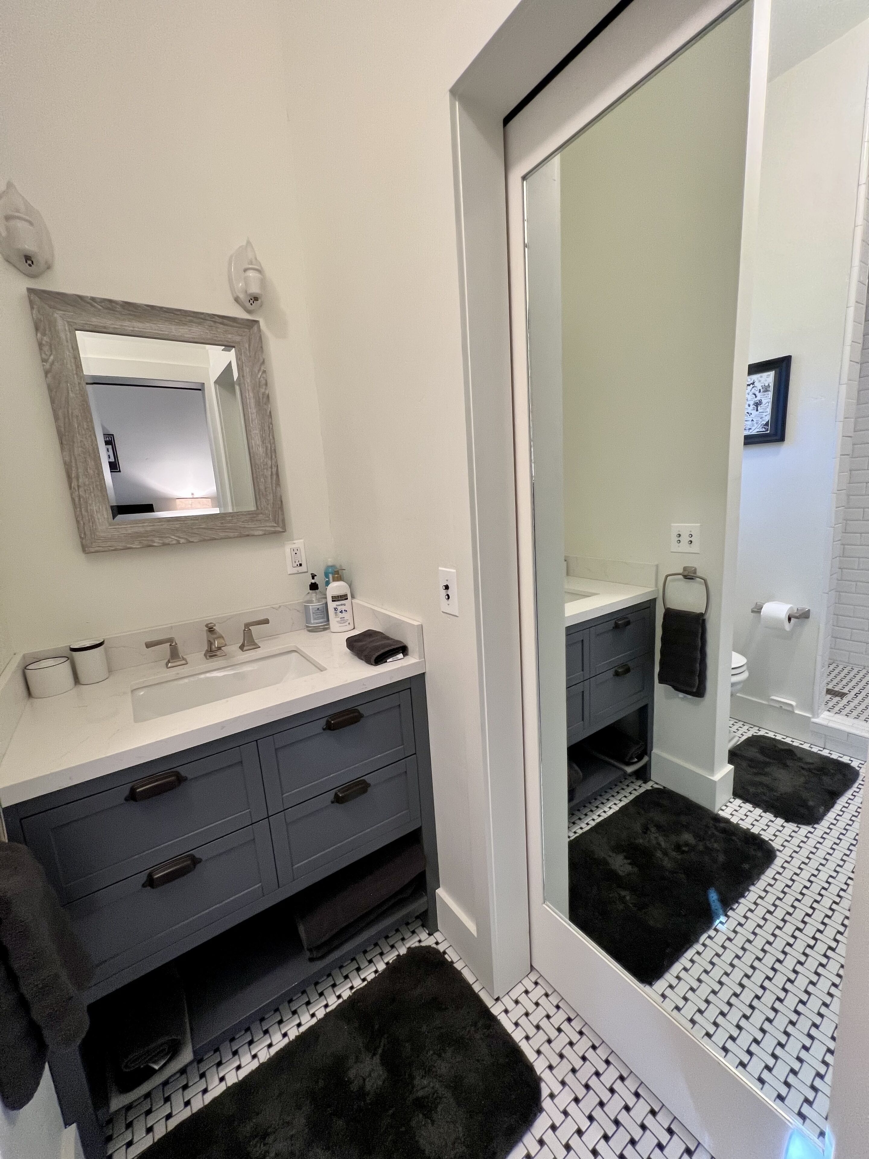 Un bagno con un lavandino bianco, mobili neri antracite, uno specchio grande e un tappeto nero.