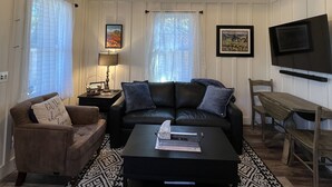 A living room with a black leather sofa, a patterned rug, a chandelier, a television, and a wooden table. - Downtown Cozy Cottage, two blocks from downtown and new! (Paso Robles)