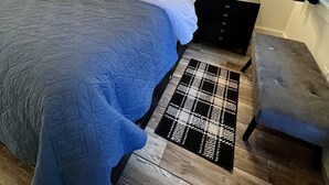 A bedroom with a large bed, two bedside tables with lamps, a headboard, a black and white patterned rug, and a small bench. - Downtown Cozy Cottage, two blocks from downtown and new! (Paso Robles)