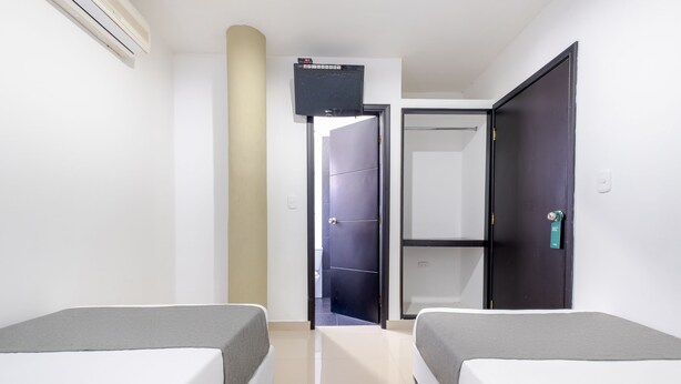Habitación de hotel con dos camas, un televisor montado en la pared, una puerta que da al baño y un armario.