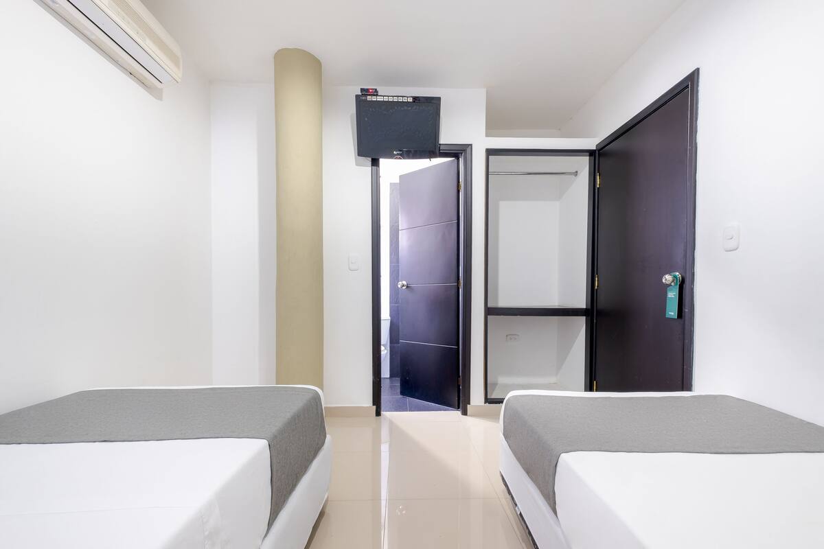 A hotel room with two beds, a TV mounted on the wall, a door leading to a bathroom, and a wardrobe.