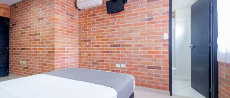 A room with a bed, a brick wall, a door, and an air conditioning unit.