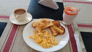 Un plato de desayuno con huevos revueltos, tostadas, una taza de café y un vaso de jugo sobre una mesa con mantel individual.