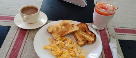 Un plato de desayuno con huevos revueltos, tostadas, una taza de café y un vaso de jugo sobre una mesa con mantel individual.