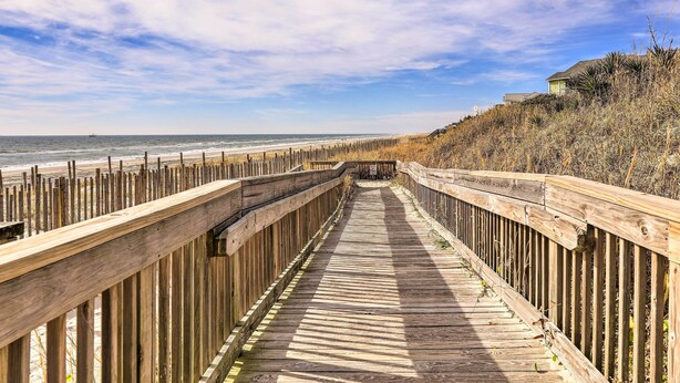 A wooden boardwalk leading to a beach with a wooden fence on one side and a building on the other. - Emerald Isle Condo w/ Indoor Pool & Beach Access! (Emerald Isle)