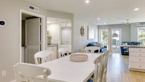 A modern kitchen with white cabinetry, a dining table with chairs, and a large window with a view of the outdoors. - Emerald Isle Condo w/ Indoor Pool & Beach Access! (Emerald Isle)