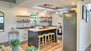Une cuisine moderne avec un îlot central, des tabourets en bois et un grand réfrigérateur.