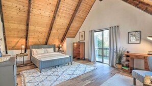 Une chambre avec un plafond en pente, un lit, un bureau et une grande fenêtre.