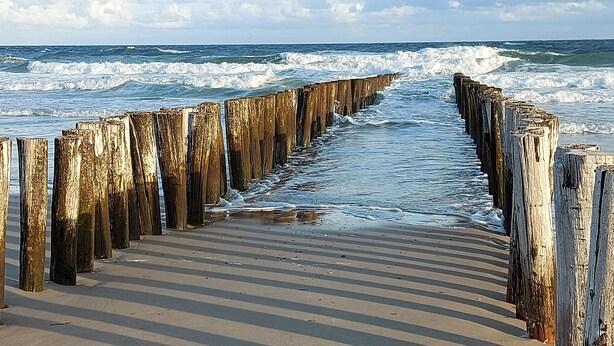Une jetée en bois qui s’avance vers l’océan, où les vagues viennent s’écraser.