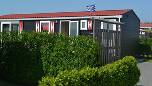 Une rangée de maisons mobiles avec un toit rouge, un drapeau au sommet et une clôture en bois à l’avant.
