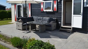 Une terrasse extérieure avec un canapé gris, une table et un parasol.