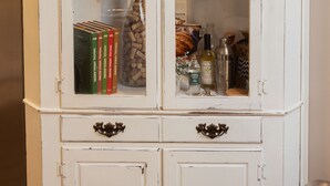 Un mueble blanco con puertas de cristal que contiene libros, un reloj y varias botellas.