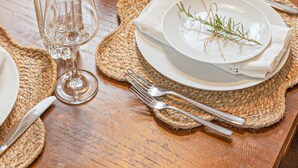 Una mesa de comedor dispuesta con platos blancos, vasos transparentes y un jarrón con flores.