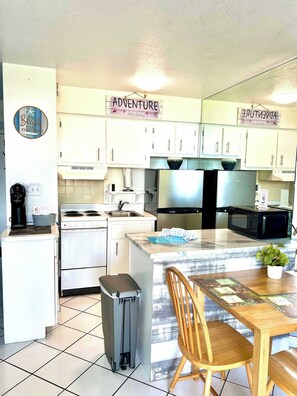 A compact kitchen with white cabinets, a stainless steel stove, a microwave, and a small trash bin.