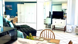 Una sala de estar moderna con un sofá, una mesa de comedor con un mantel individual, un microondas y un televisor.