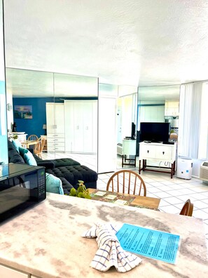 A modern living room with a sofa, a dining table with a placemat, a microwave, and a television.
