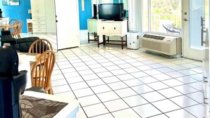 Una sala de estar con televisión, un mueble blanco y un ventanal.