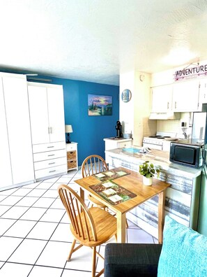 A compact kitchen with white cabinets, a dining table with chairs, a microwave, and a small potted plant.
