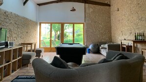 Un vaste espace de vie comprenant une table de billard, des sièges confortables, un téléviseur et une vue sur l’extérieur grâce à de grandes fenêtres.